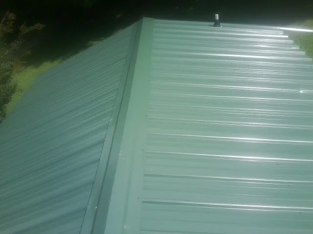New green metal panels meeting at the ridge of a roof — Flat Roof Repair work by our crew in Huron